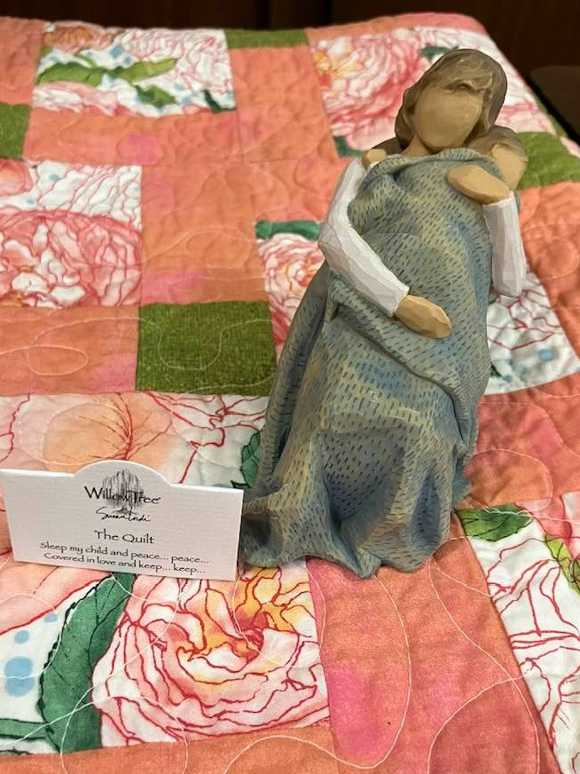 The Quilt, sculpted figure by Susan Lordi,  Handmade floral quilt by El Paso Northeast Quilters Guild member Colleen Hughes