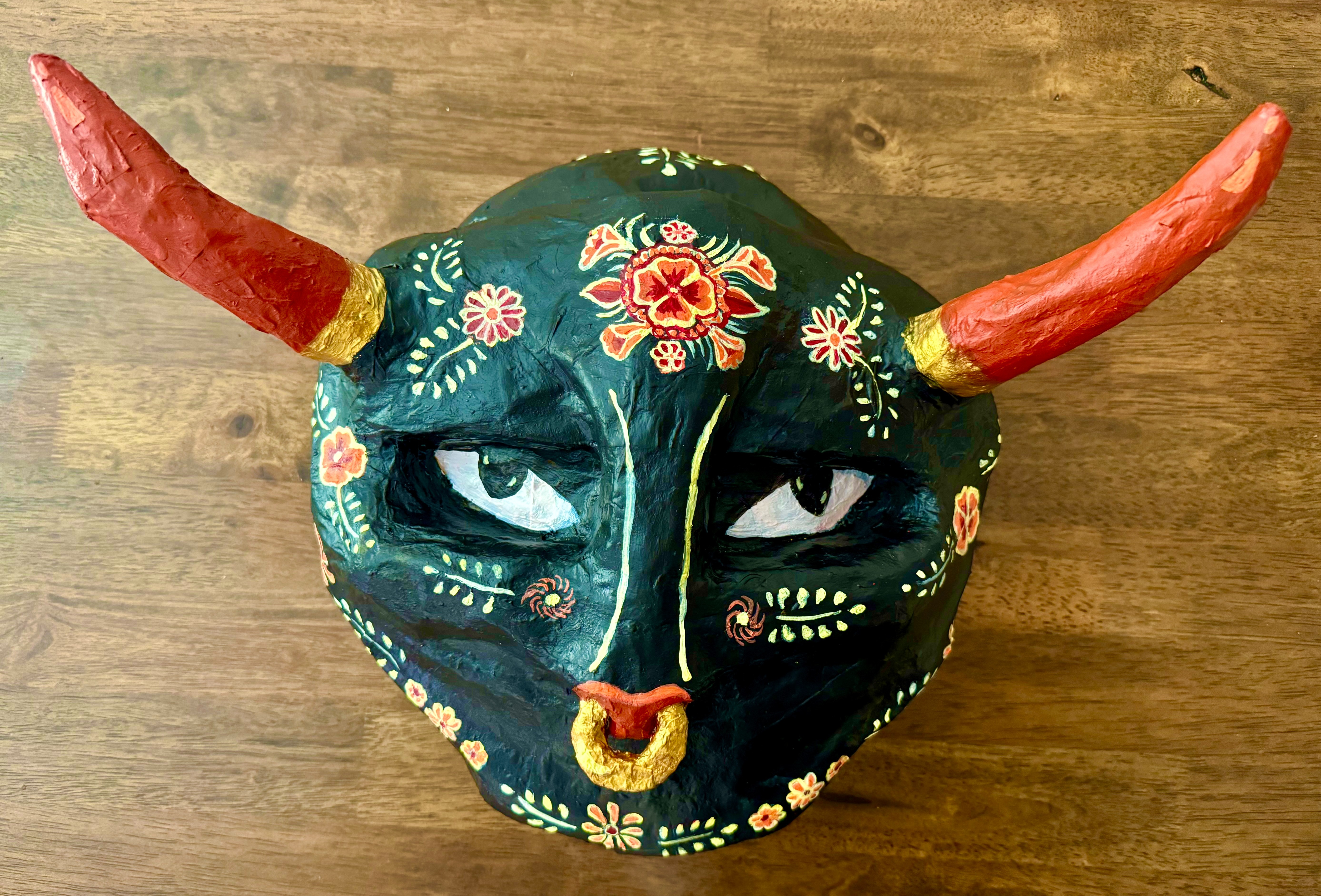 LxsDos + Xingaderas, “Torito de Olinalá; Mexican papier-mâché and acrylic paint.  August, 2024. | La máscara representa la riqueza cultural de  las personas que han sido desplazadas de sus países de origen, así como su fuerza, sus tradiciones y su belleza. En contraste a las narrativas que predominan en Estados Unidos acerca de las personas que buscan refugio en este país.   The mask represents the cultural richness of displaced peoples, as well as their strength, their traditions and beauty. In contrast to the dominant narratives in relation to refugees.